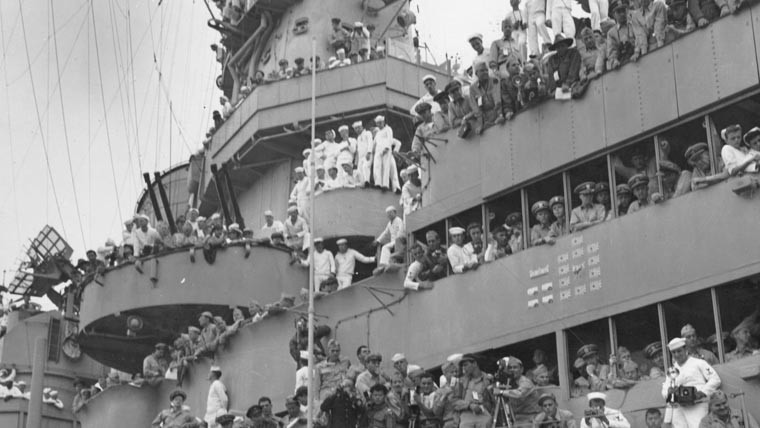 Black & white photo of uniformed men crowding the deck of a U.S. Navy ship