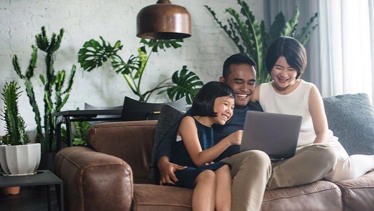A multiracial family sitting on a couch and smiling at an image on their laptop